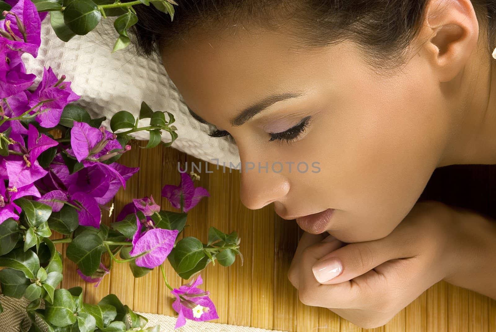 a nice portrait of young and cute brunette layng down on a wood carpet with flowers near her