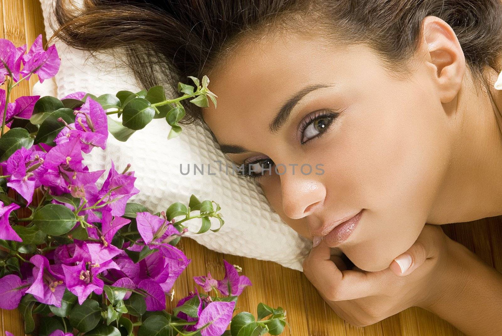 a nice portrait of young and cute brunette layng down on a wood carpet with flowers near her