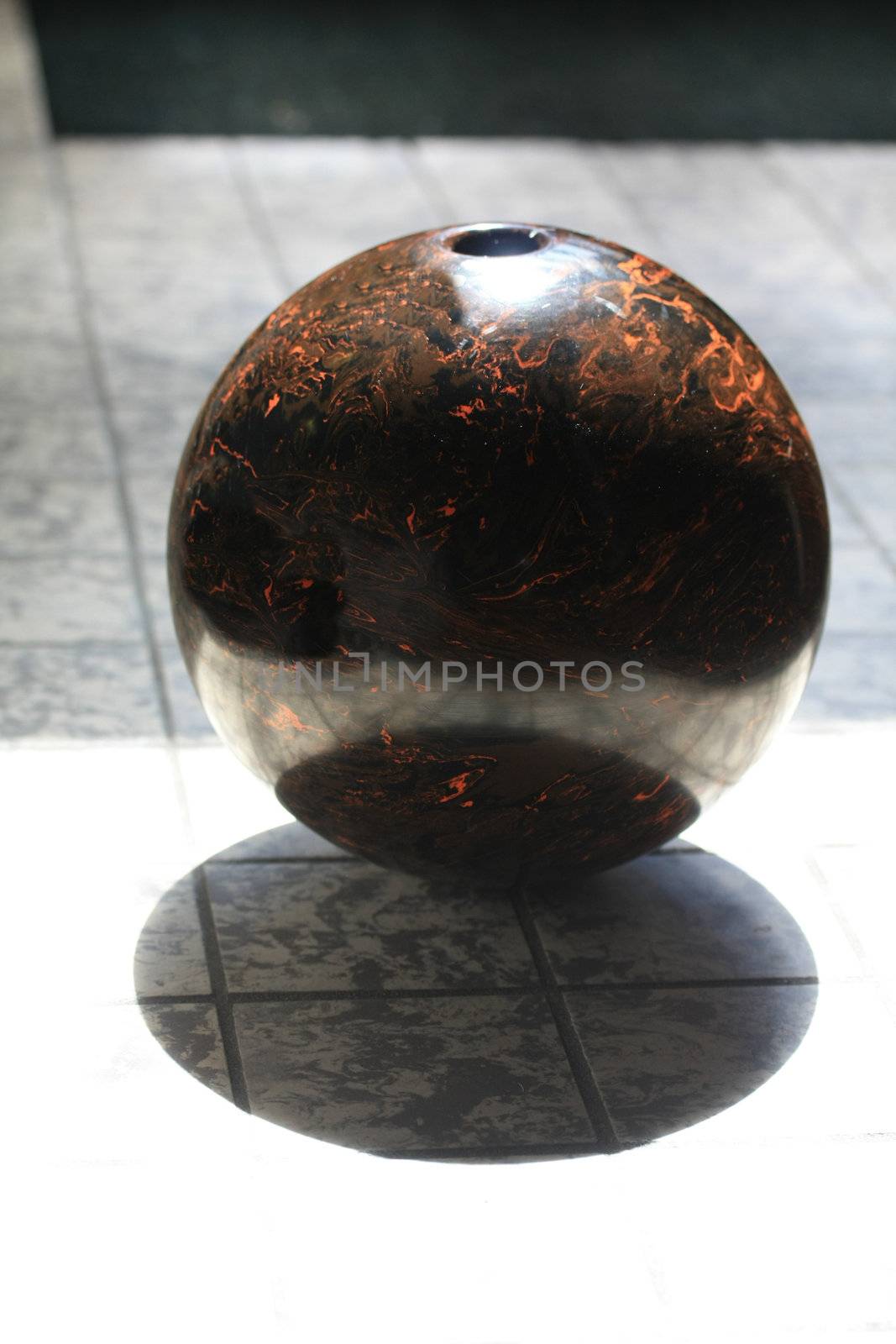 A small brown bowling ball in the sunlight producing its own shadow