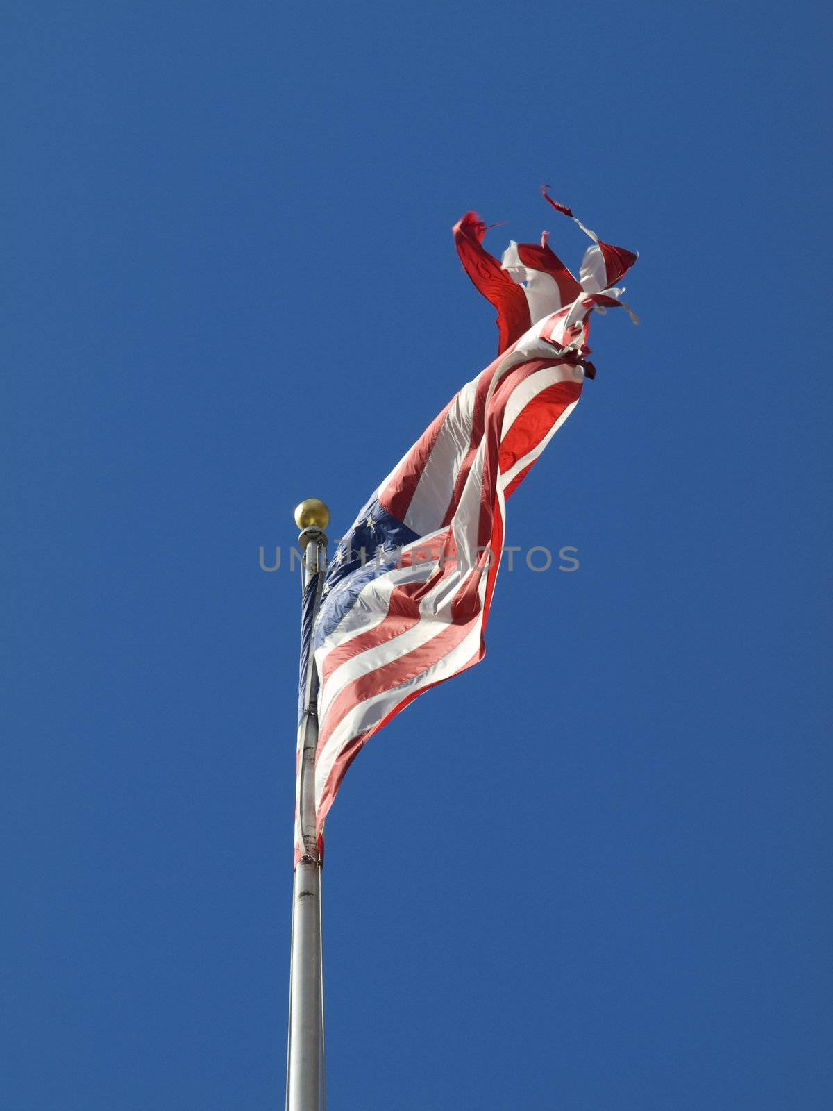 A ripped american flag waving over a blue sky.