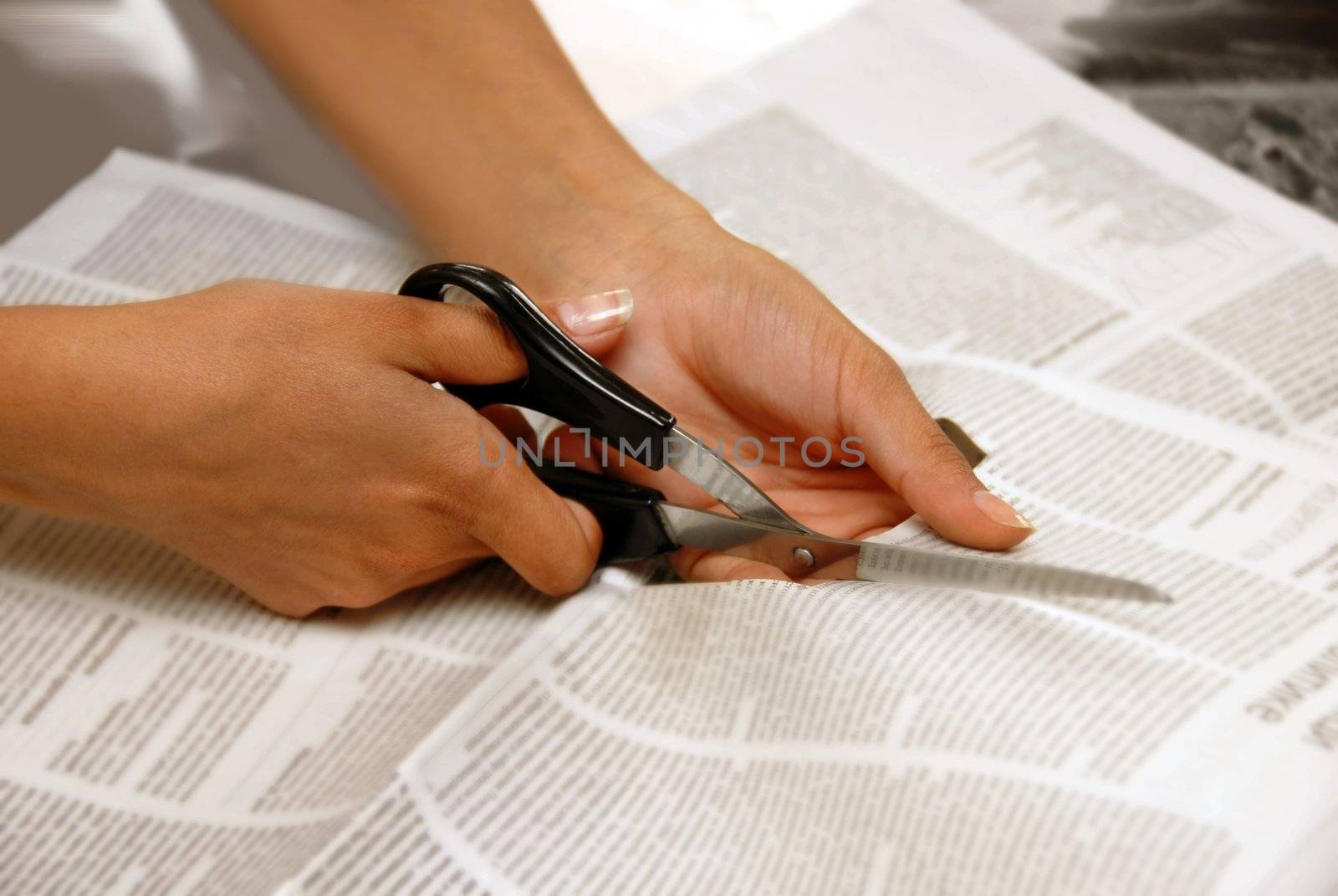 hand with scissors cutting out an article from newspaper