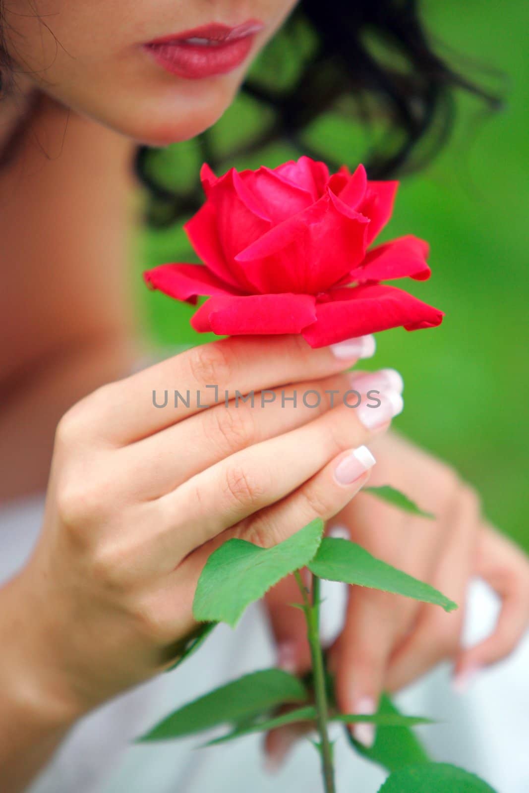 Young woman with red rose, green nature background, Focus on rose in foreground.