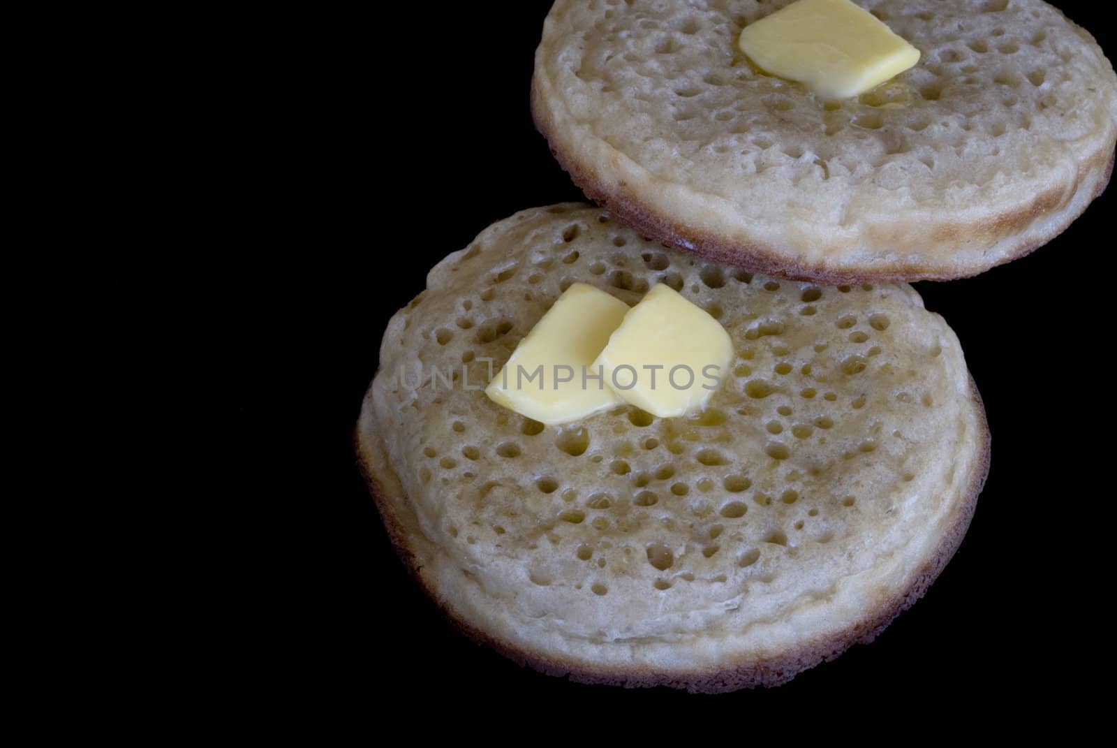 two buttered crumpets, isolated on a black background