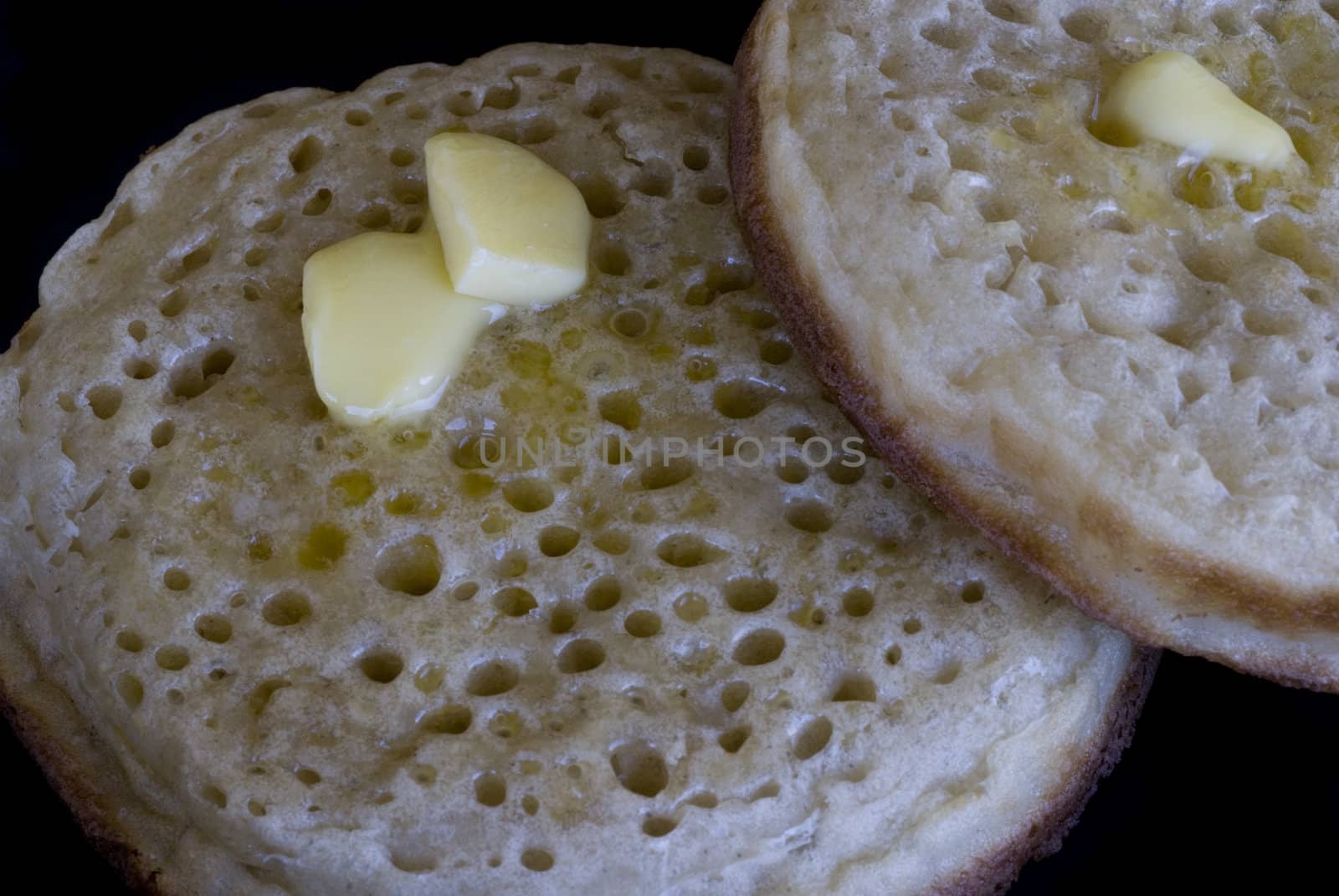 two buttered crumpets, isolated on a black background