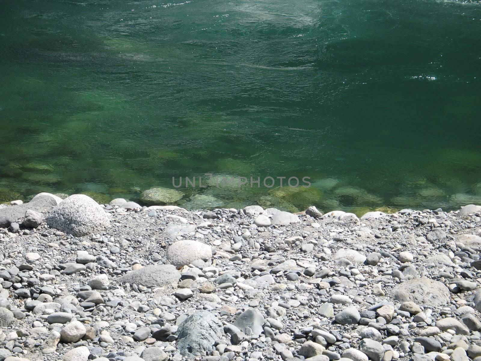 grey polished rocks and green river water by mmm
