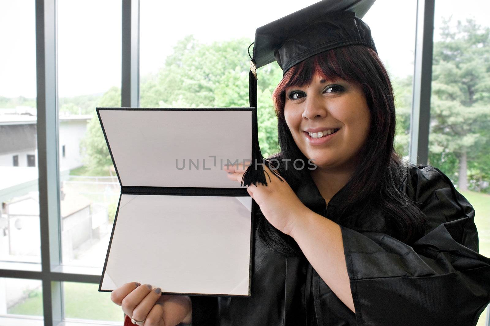 A student that recently had a school graduation posing proudly with her diploma indoors.