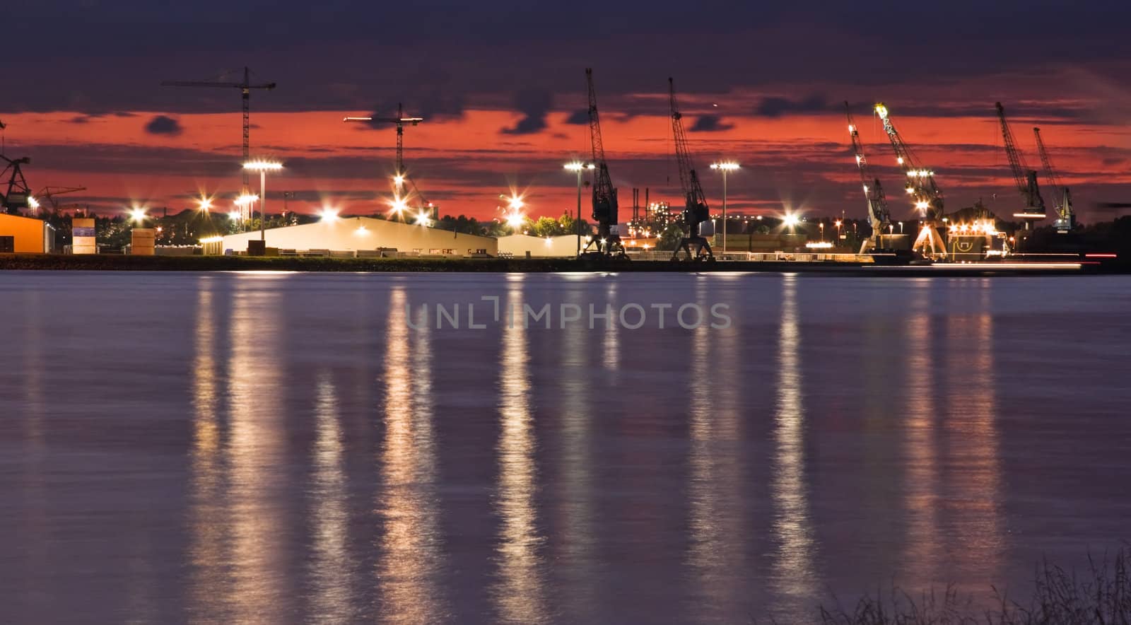 Container port with cranes at the riverside after sunset