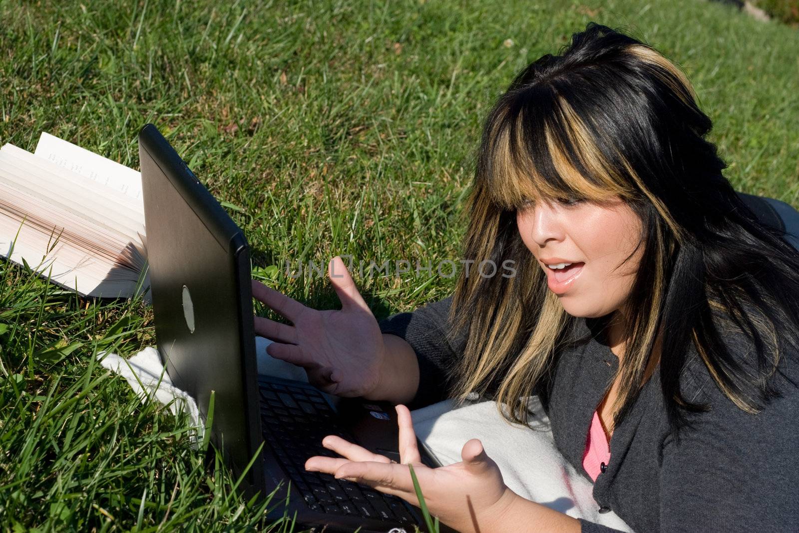 A young student using her laptop computer while laying in the grass on a nice day.