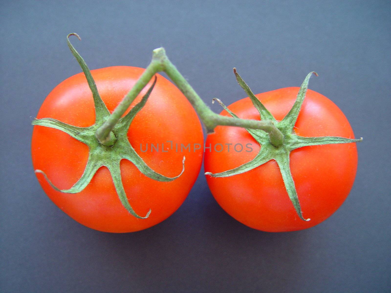Two bright red tomatoes on black background.