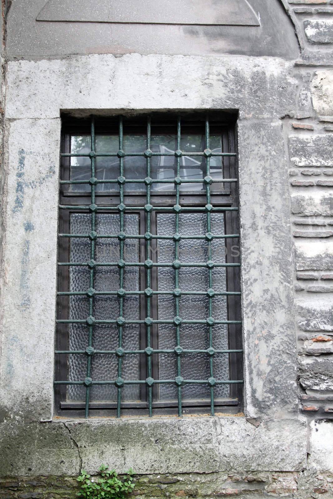 Ancient curch window with metal grating on background with gray stone wall