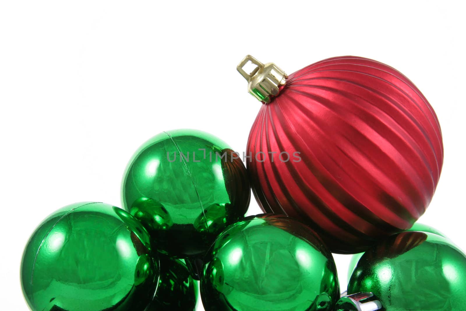 A red bauble sitting on a bunch of green Christmas baubles against a white background.
