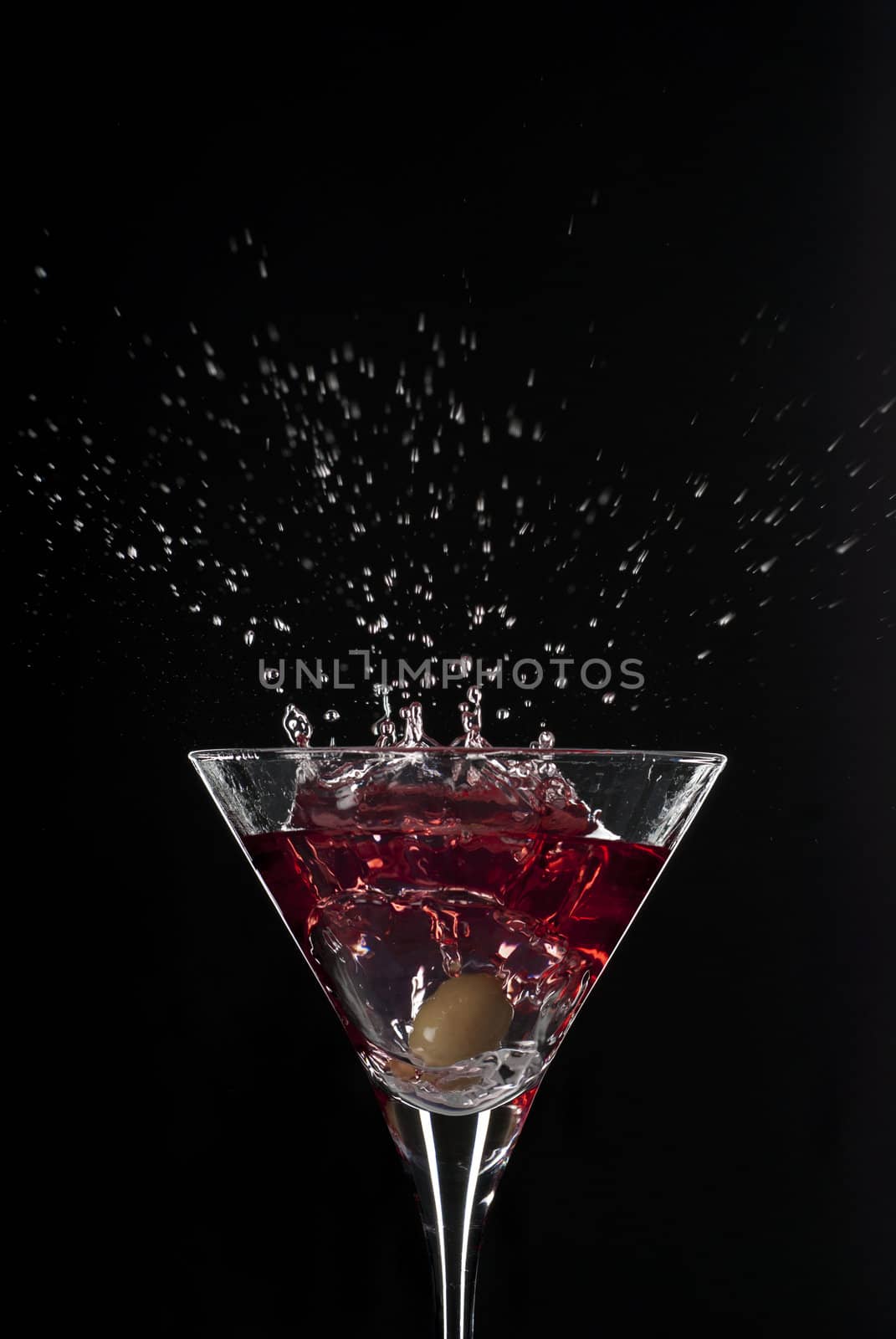 Cocktail splash with an olive on red martini with black background