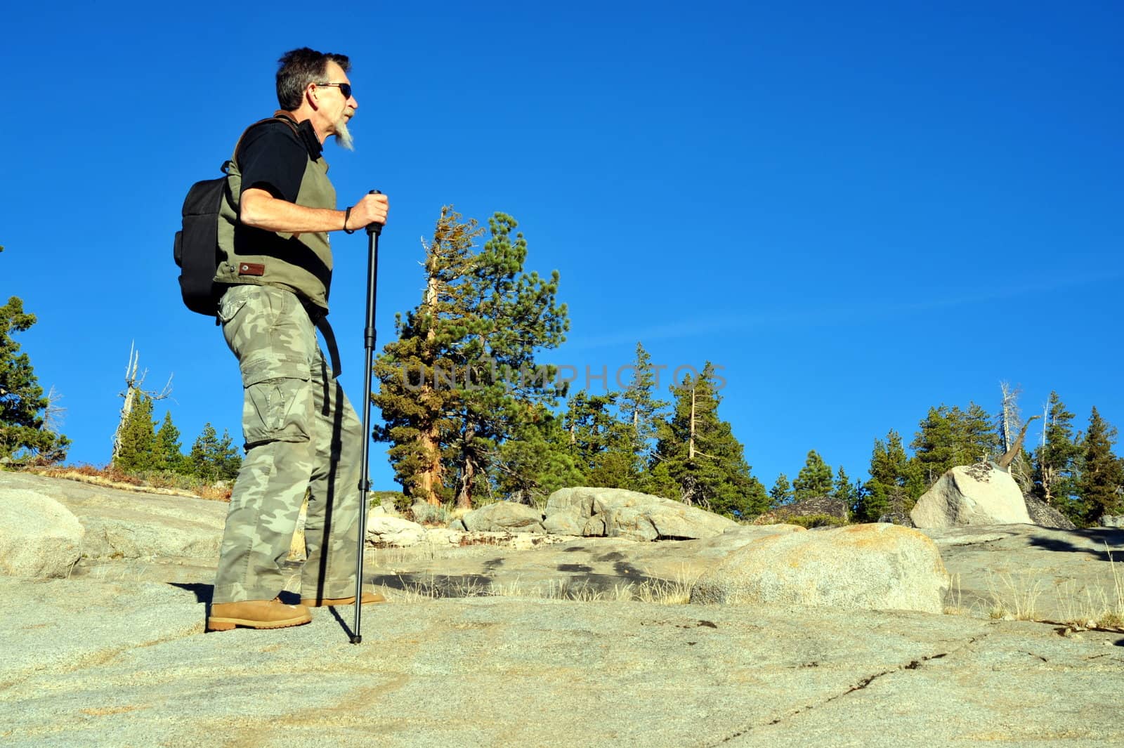 A single male day hiker reaches the summit of a granite mountain to