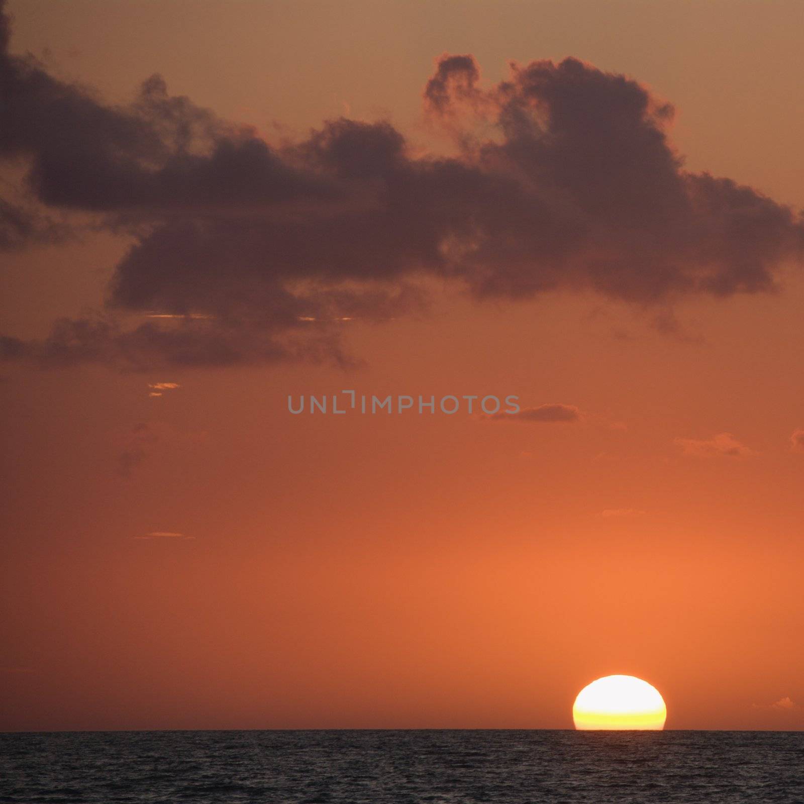 Sun setting over horizon of ocean.