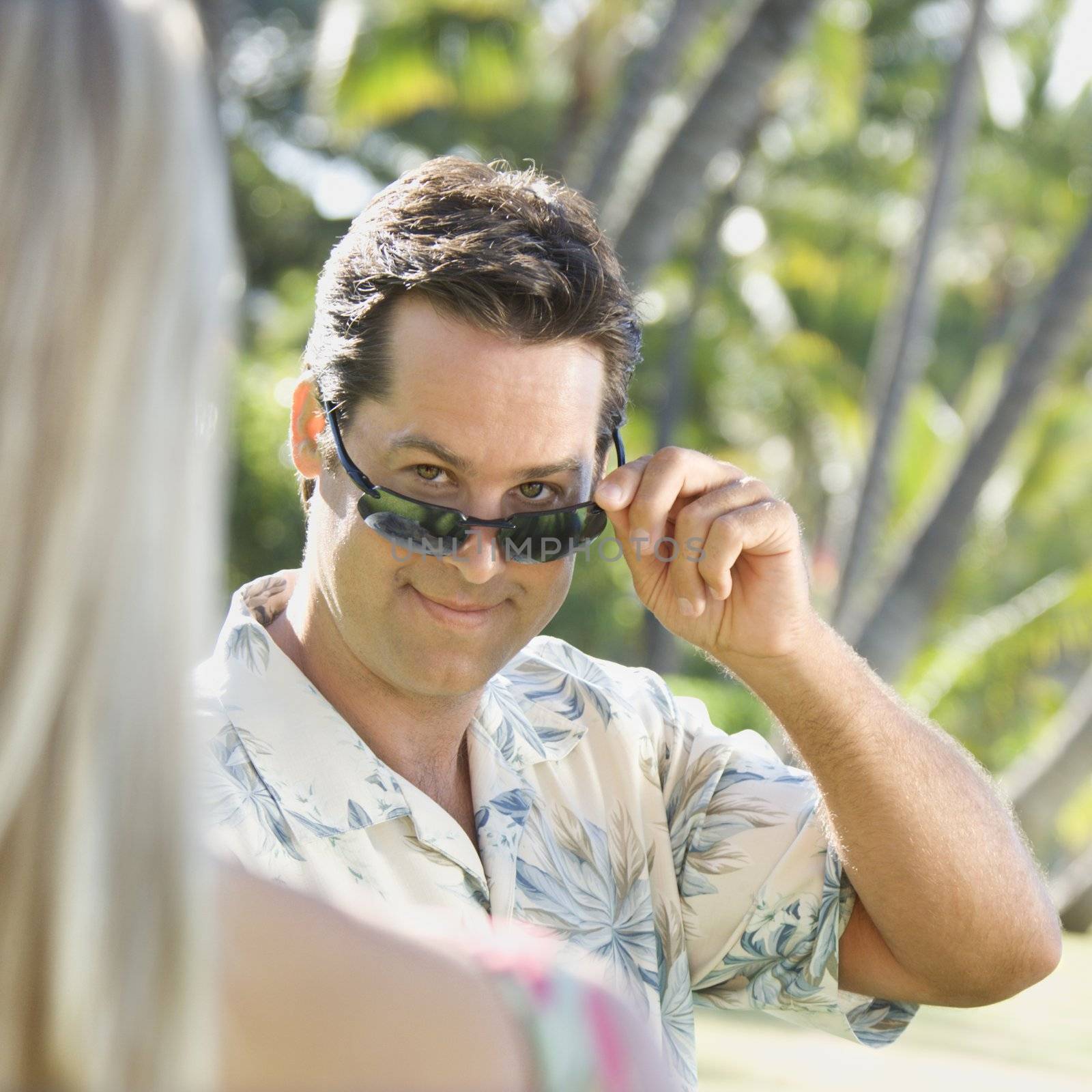 Caucasian mid adult man tilting sunglasses at woman.