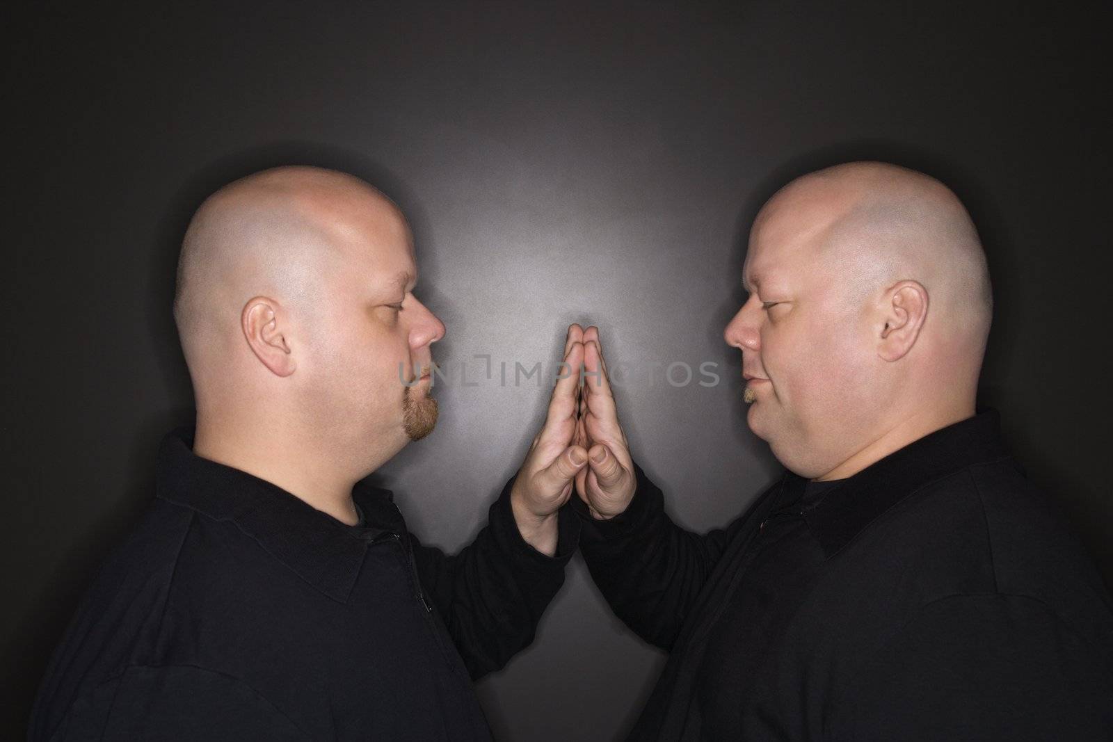 Caucasian bald mid adult identical twin men standing face to face with hands touching.