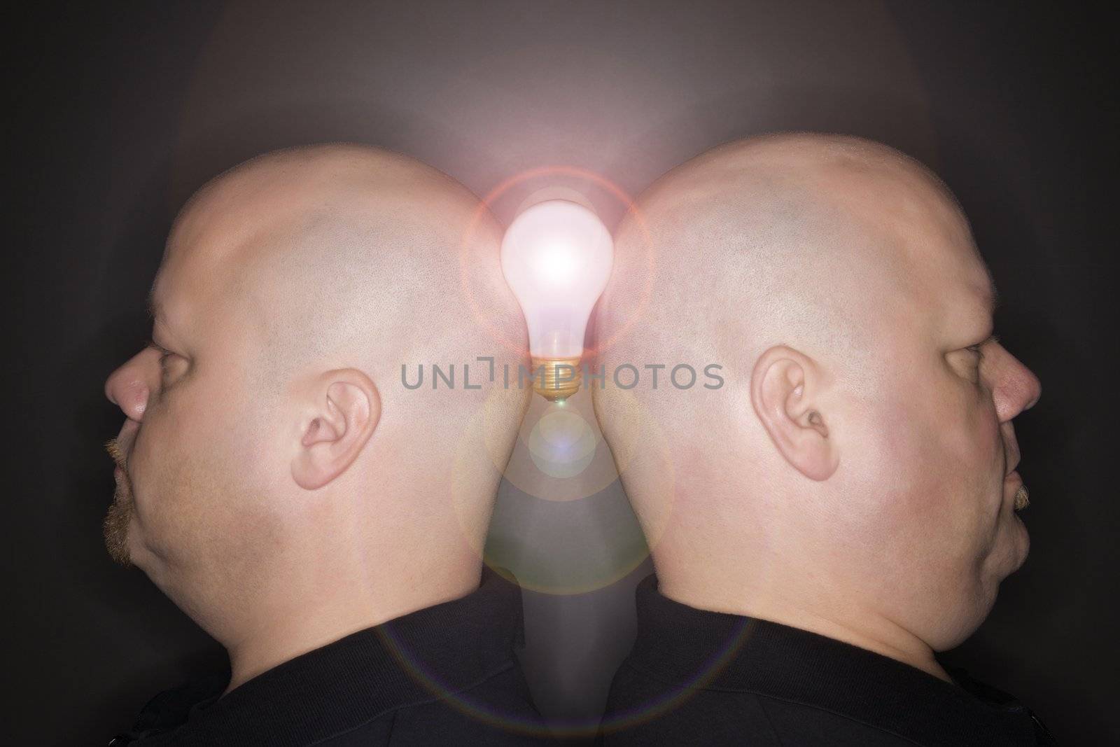 Caucasian mid adult identical twin men standing back to back and balancing a lightbulb between them.