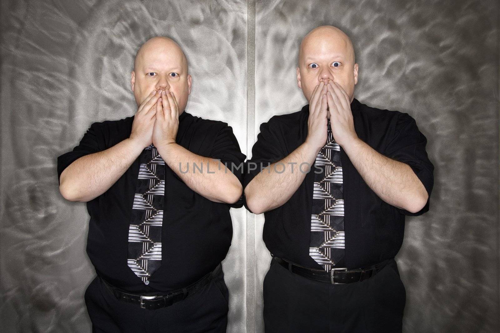 Caucasian bald mid adult identical twin men gasping with hands over mouth.