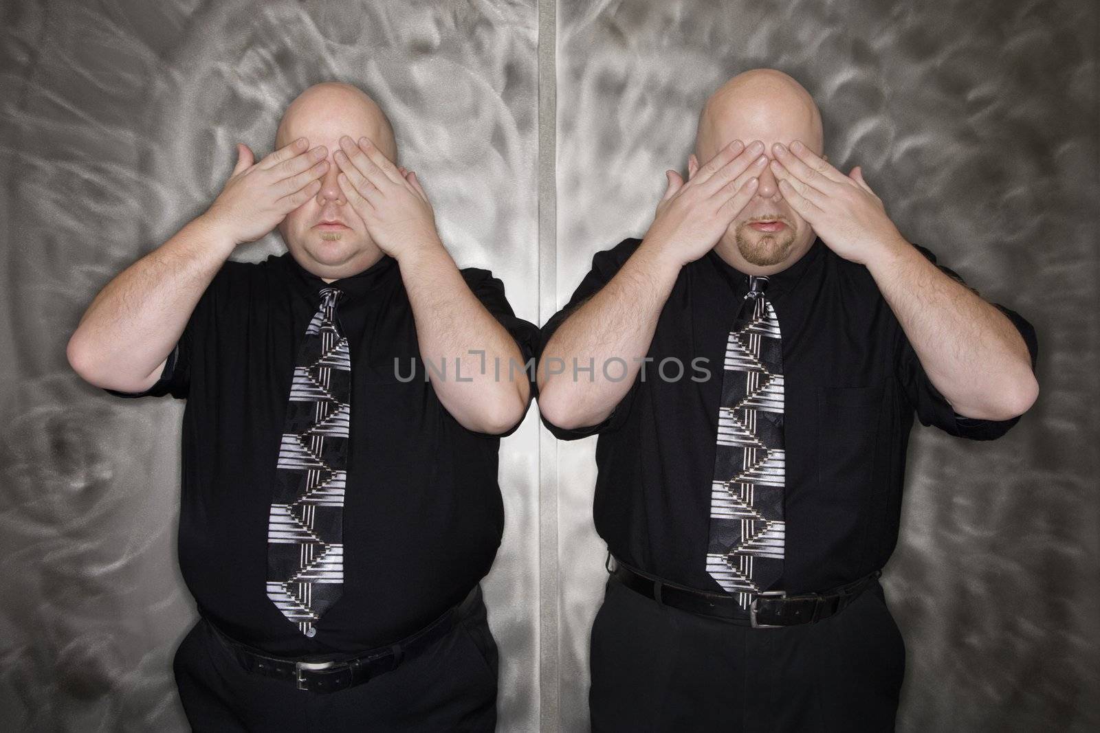 Caucasian bald mid adult identical twin men standing with hands covering eyes.