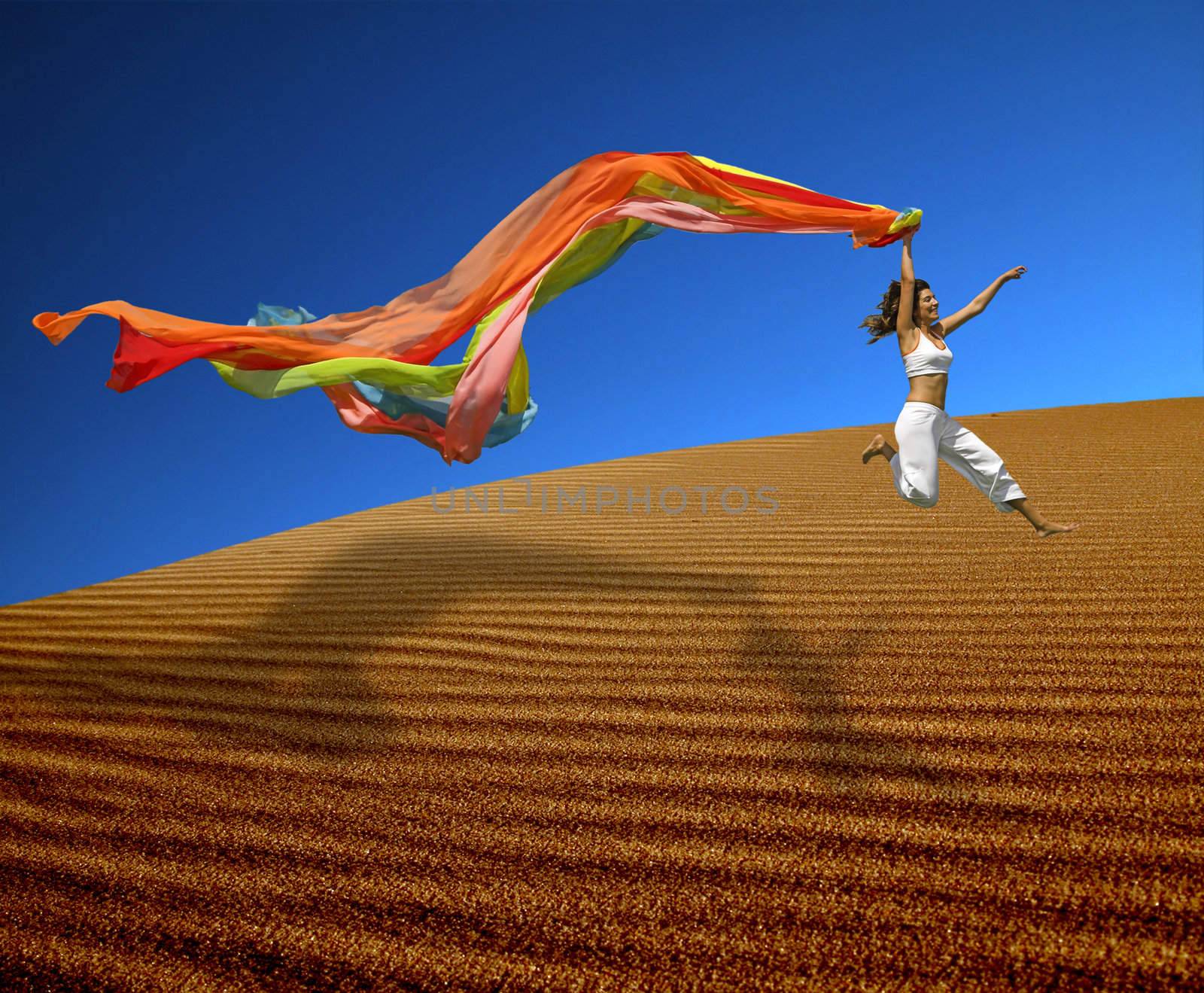 Beautiful woman jumoping over the sand dunes with a colored scarf