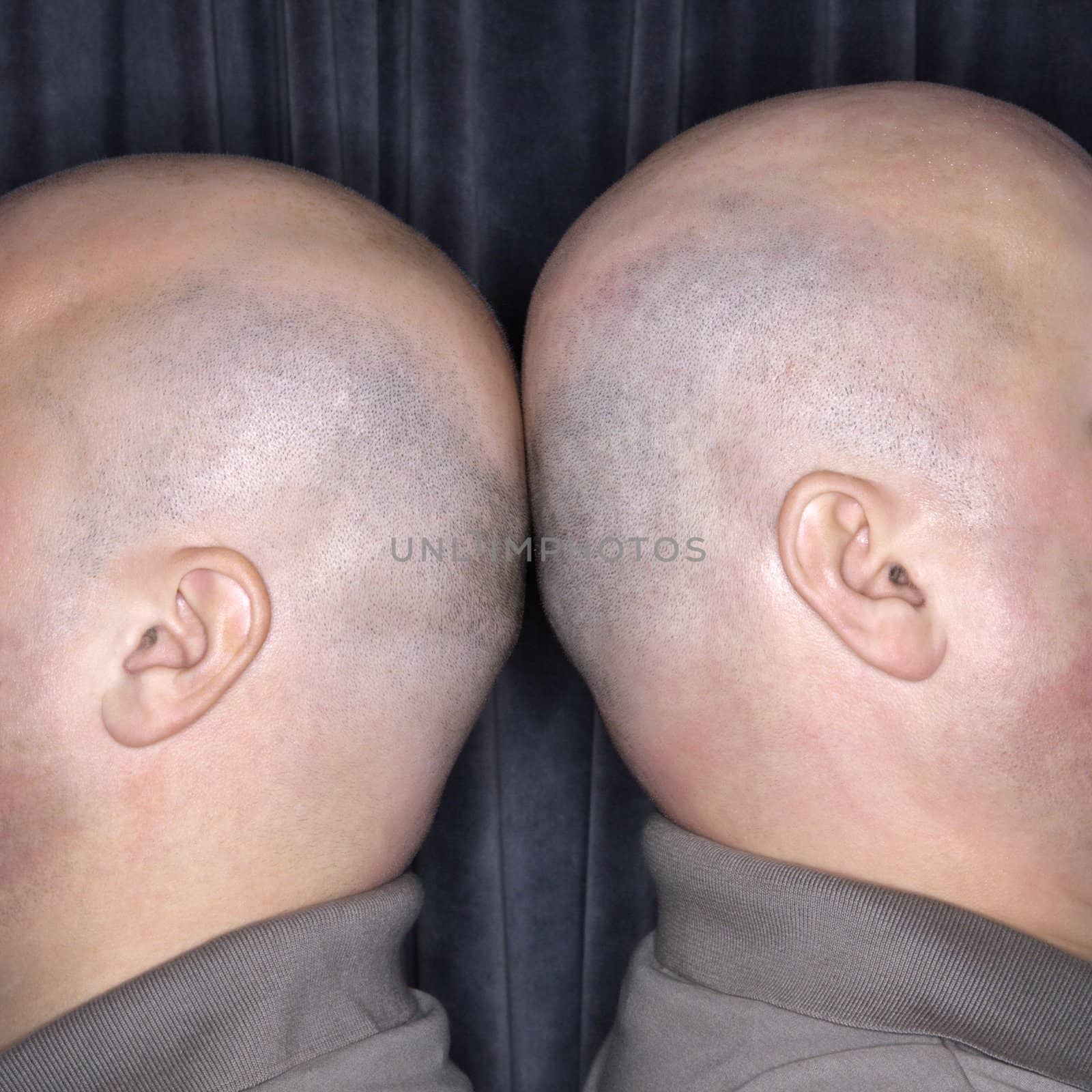 Close up of Caucasian bald identical twin men standing back to back.