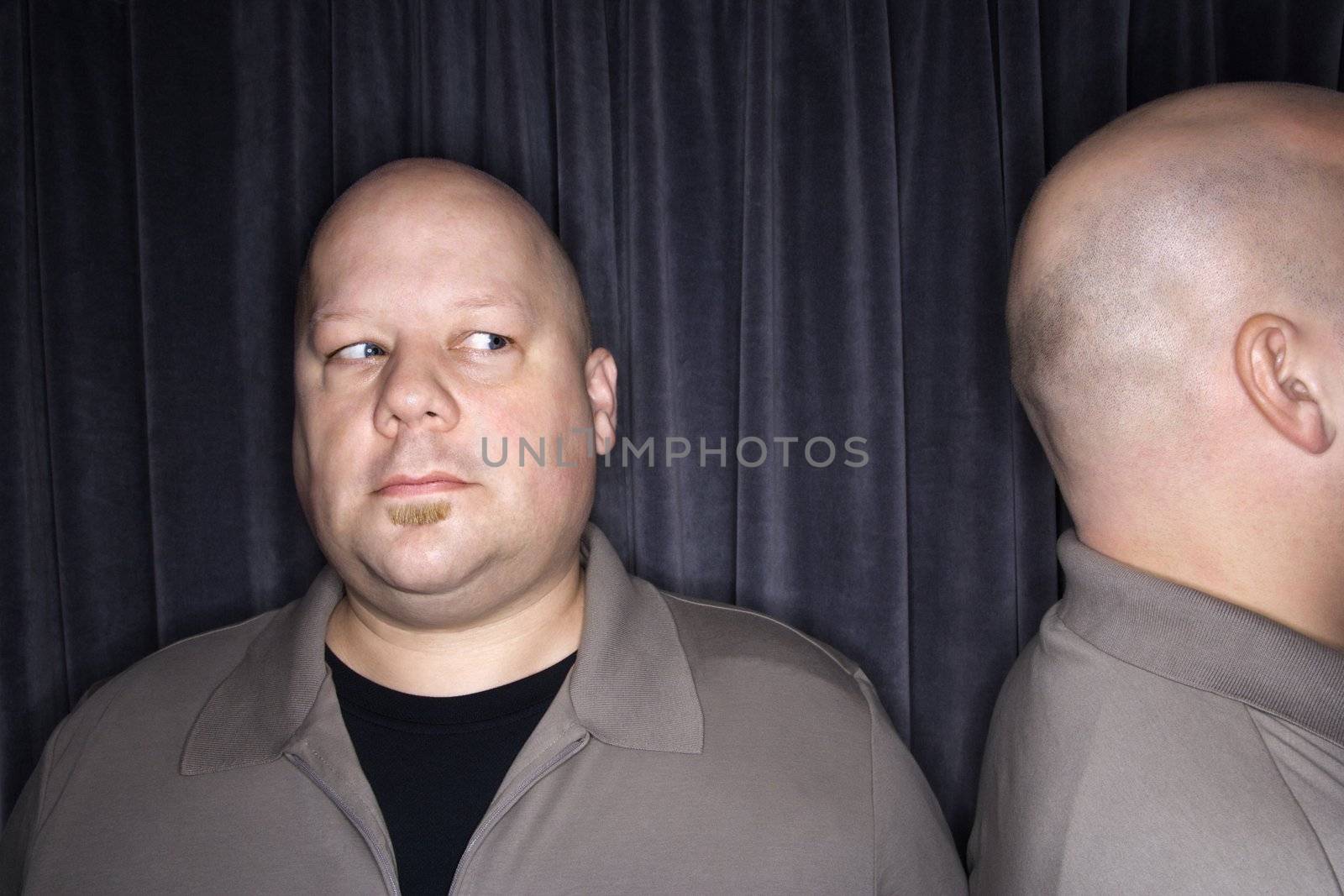 Caucasian mid adult bald man looking to side at his identical twin.