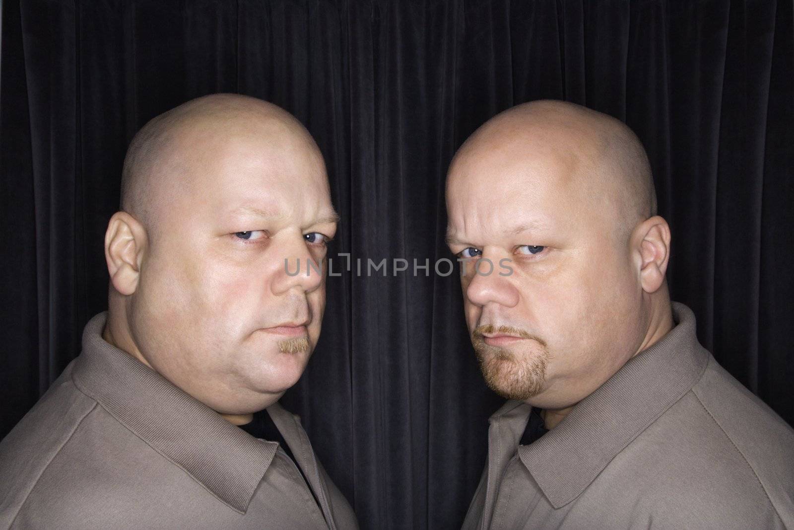 Caucasian bald mid adult identical twin men looking sternly at viewer.