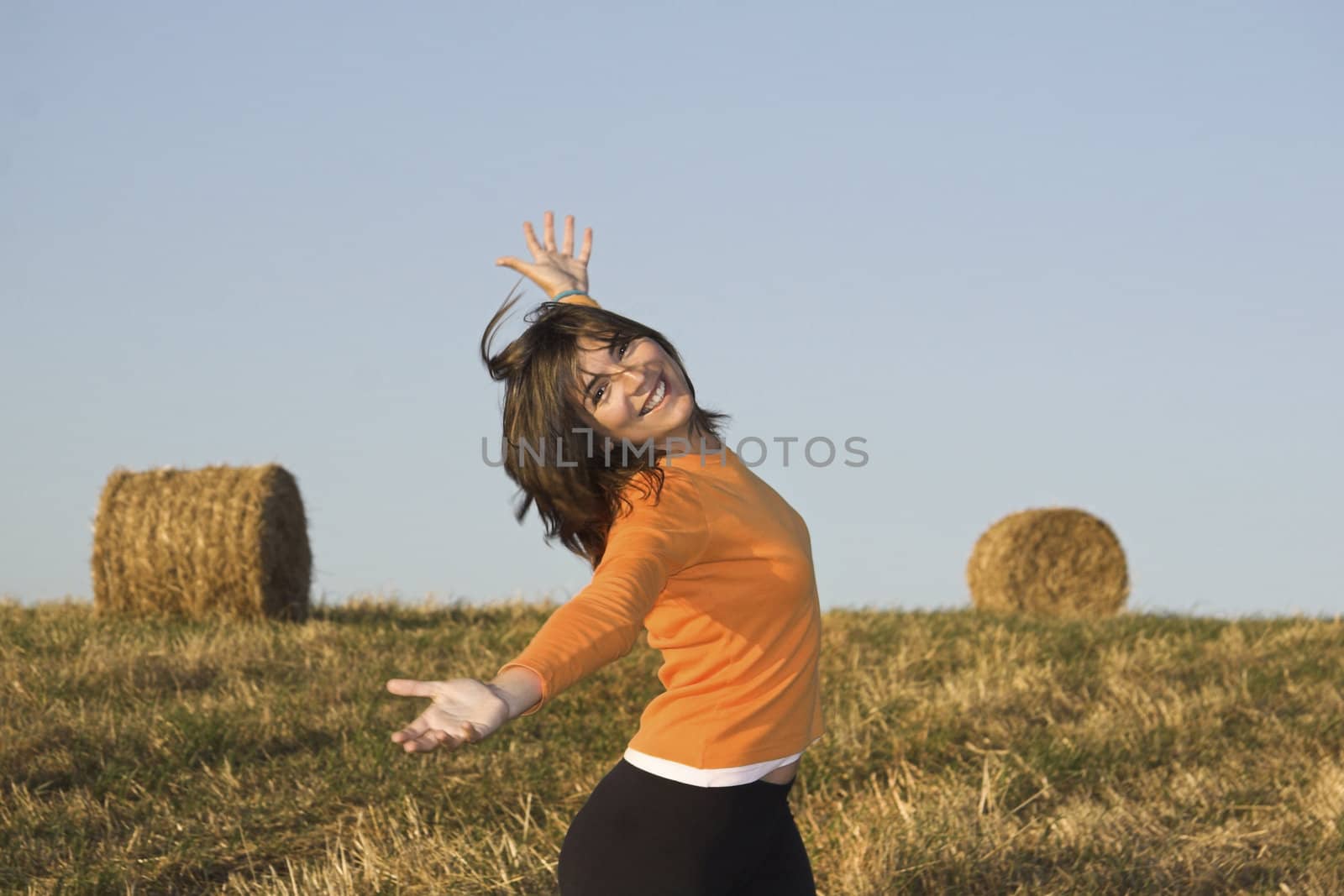 Beautiful woman open is arms  in a field with hay bales by Iko