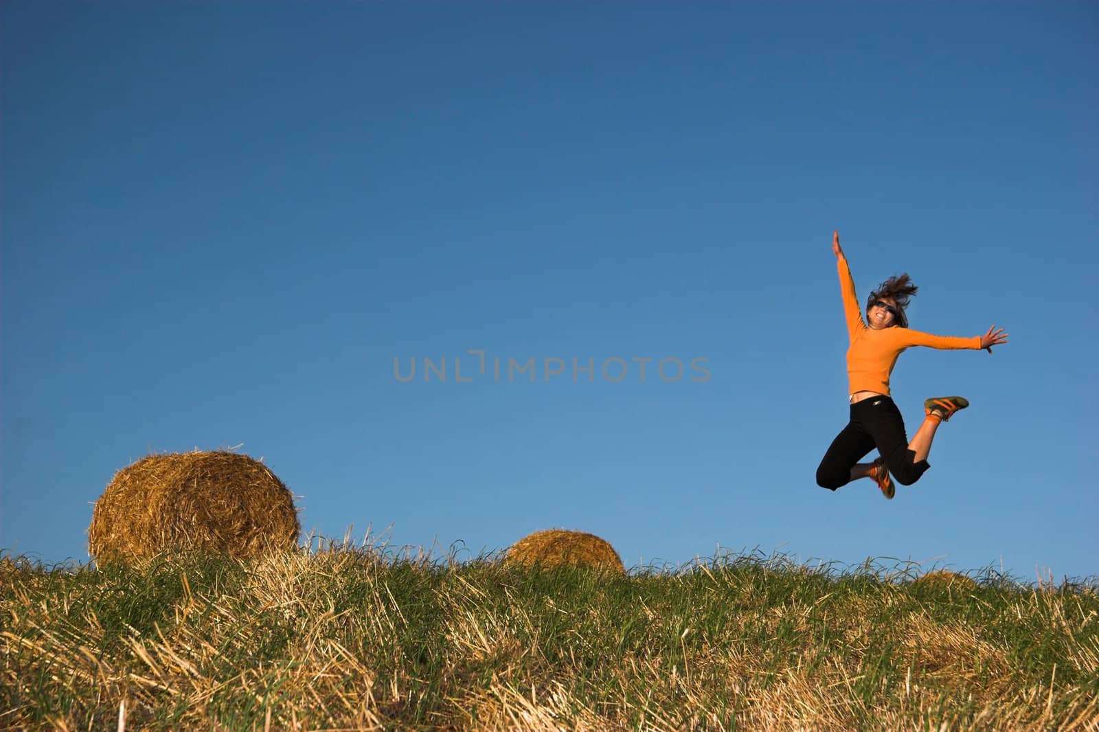 Woman jumping in a hay bales field