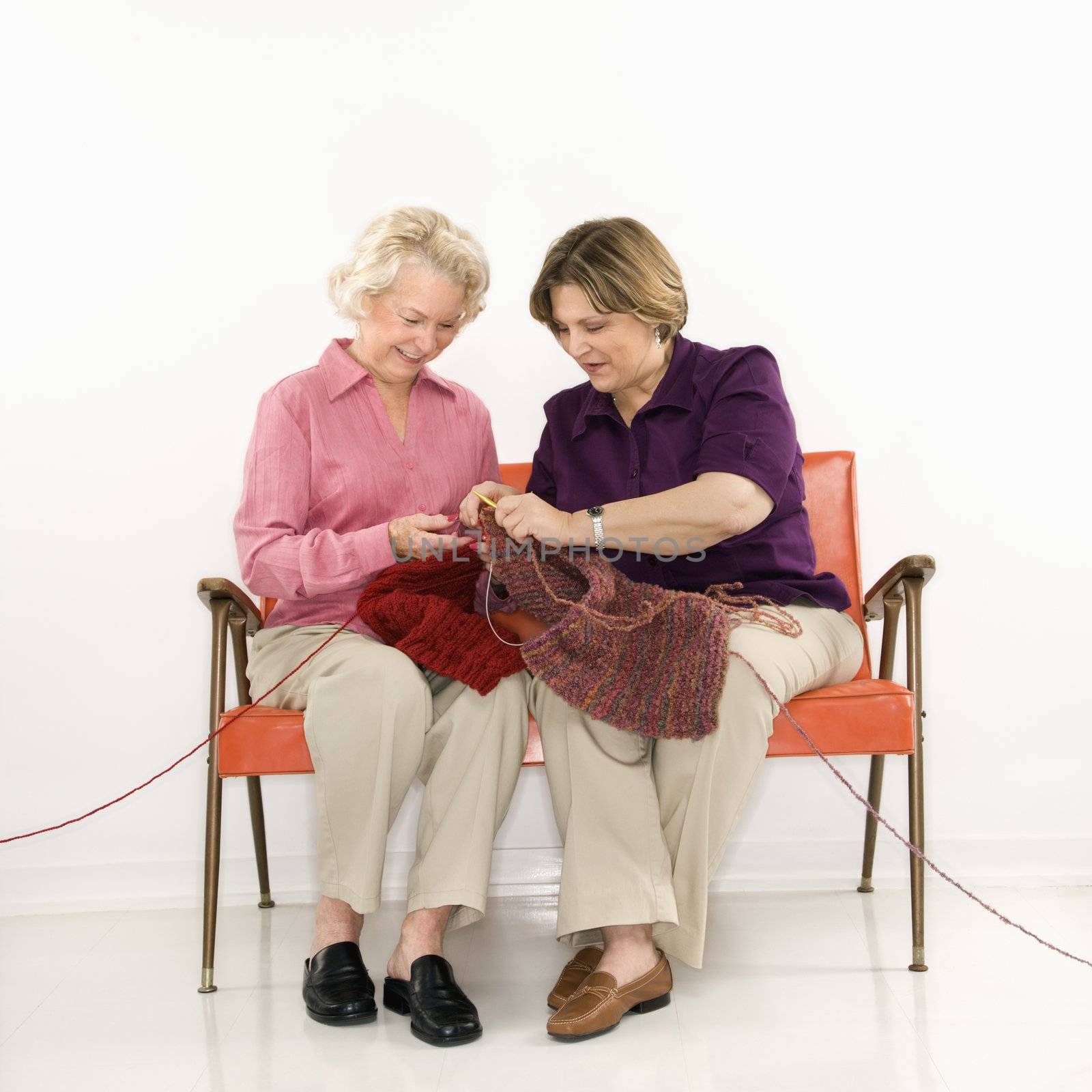 Caucasian middle aged woman and senior woman sitting and knitting.