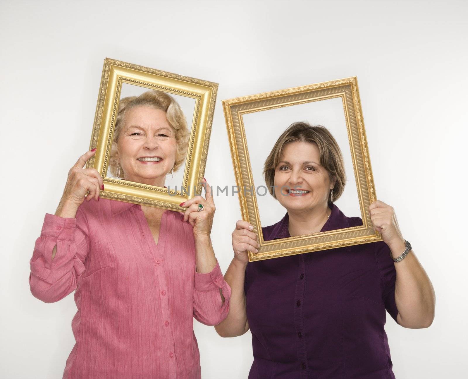 Caucasian middle aged woman and senior woman holding picture frames over faces.