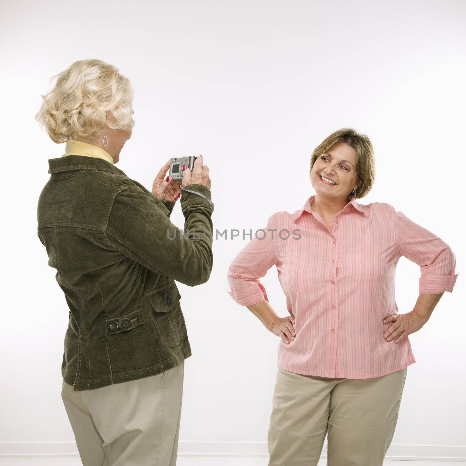 Caucasian senior woman taking photo with digital camera of middle aged woman.