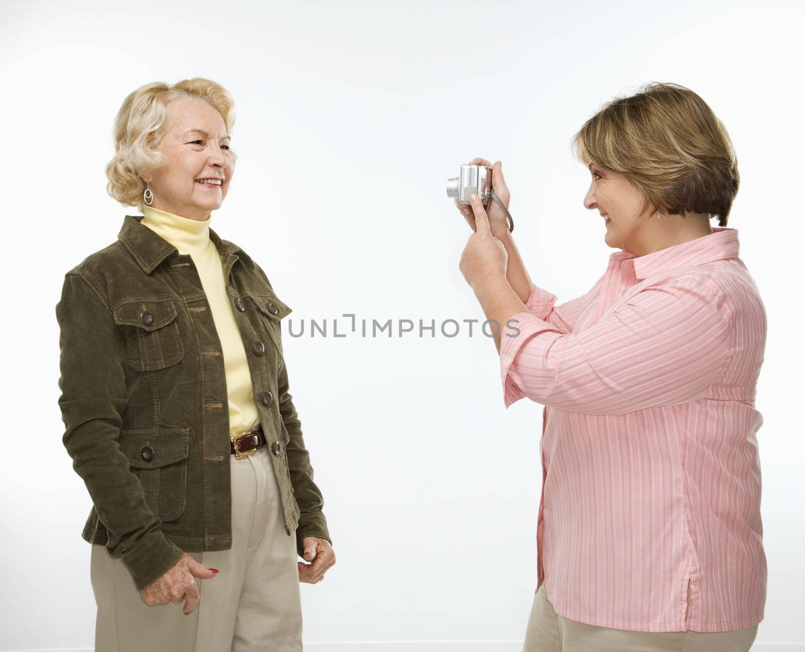 Caucasian middle aged woman taking photo with digital camera of senior woman.