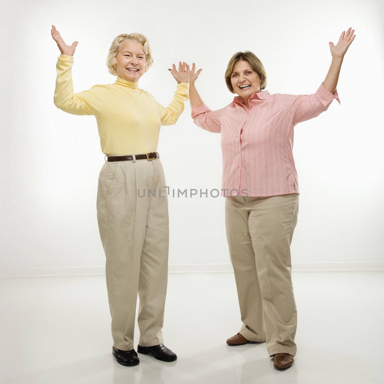 Caucasian senior woman and middle aged woman with arms in air.