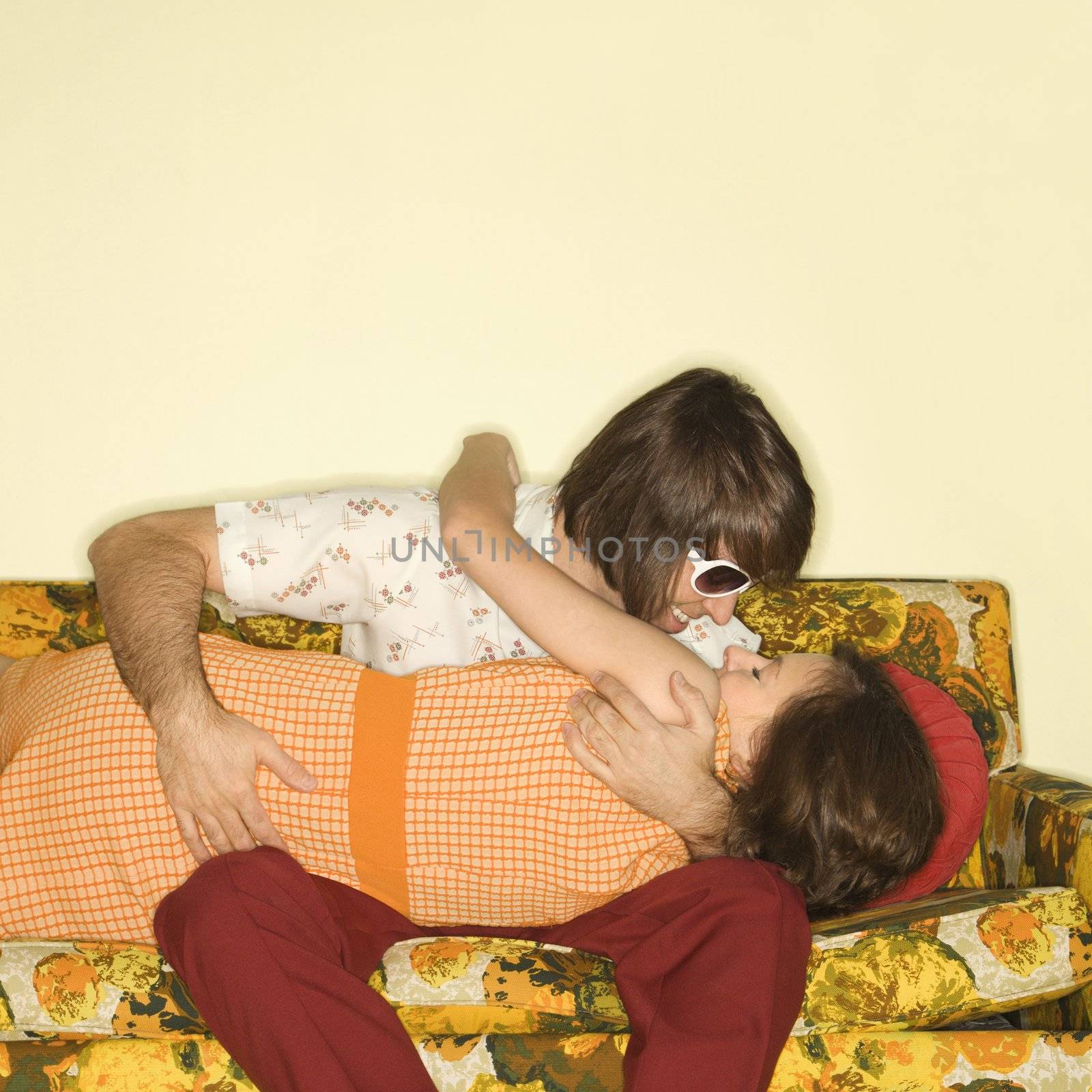 Caucasian mid-adult couple smiling and embracing on colorful retro sofa.