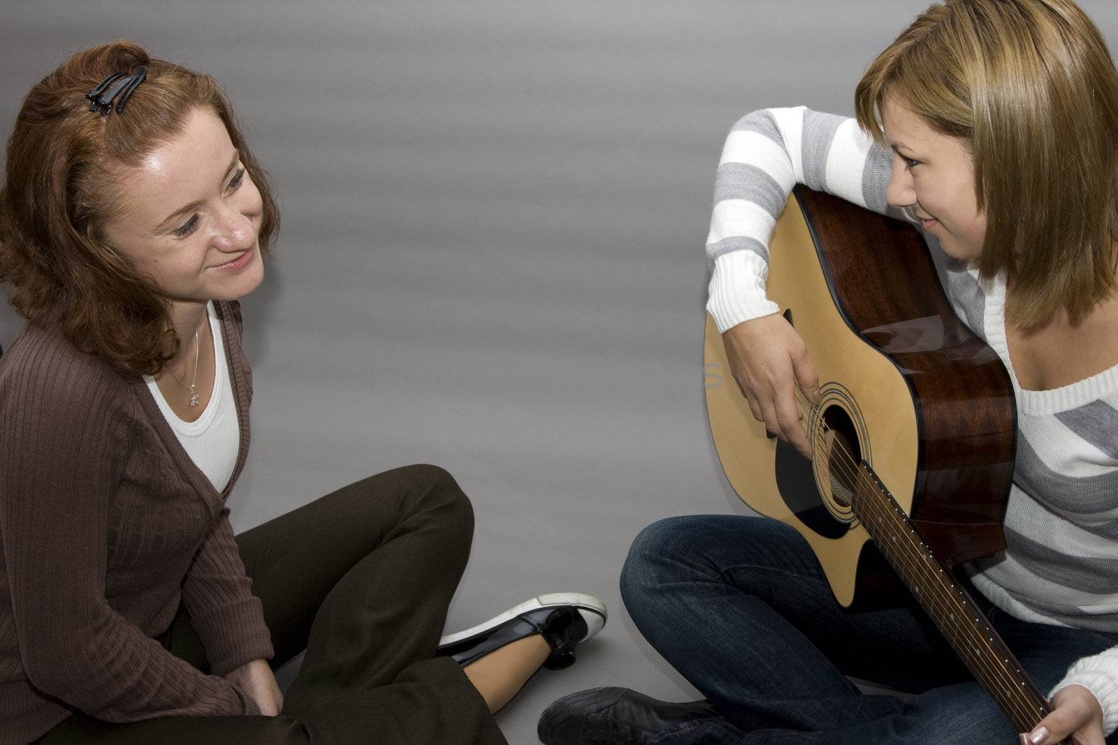 two girls. one girl playing guitar and the other one listening