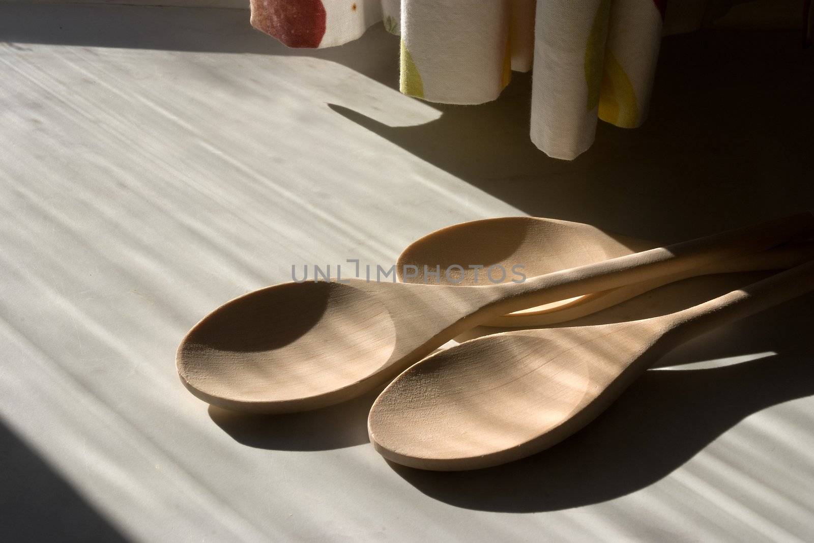 Three wooden spoons in sunlight and shadow on a kitchen work surface