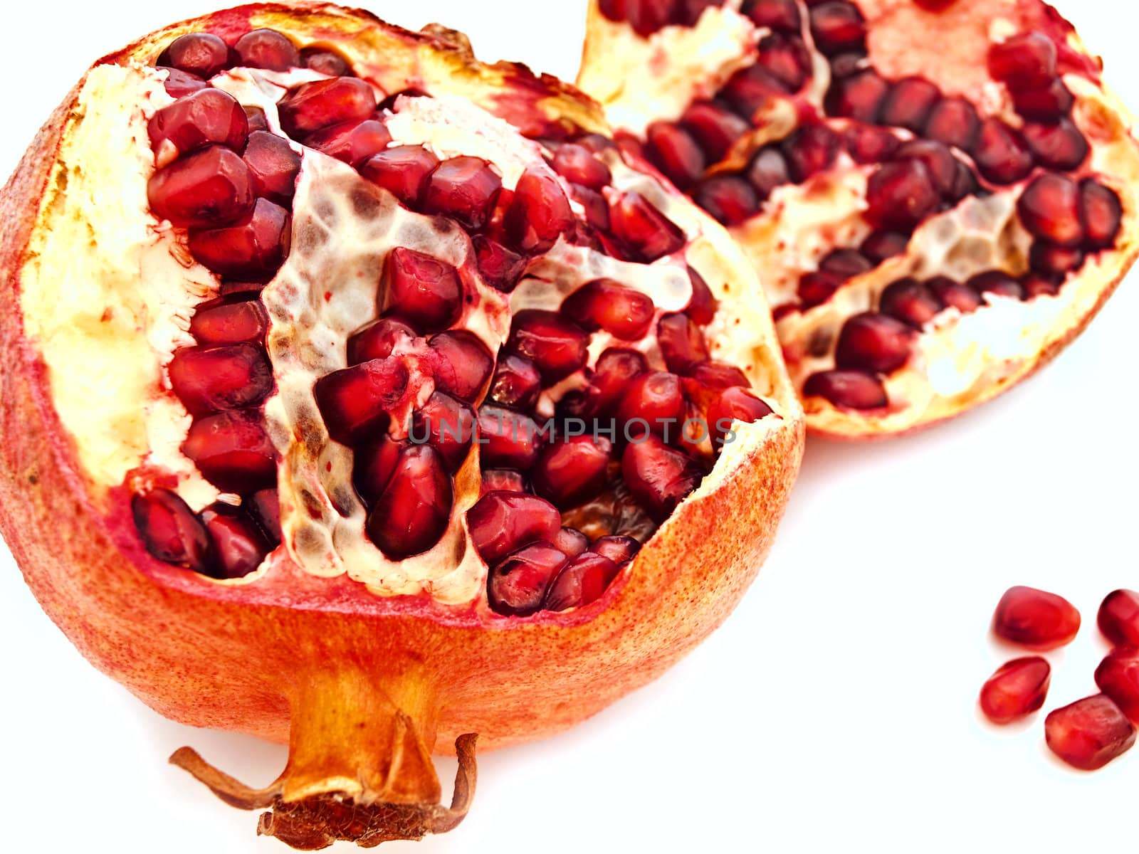 broken red pomegranate and seeds against white background 