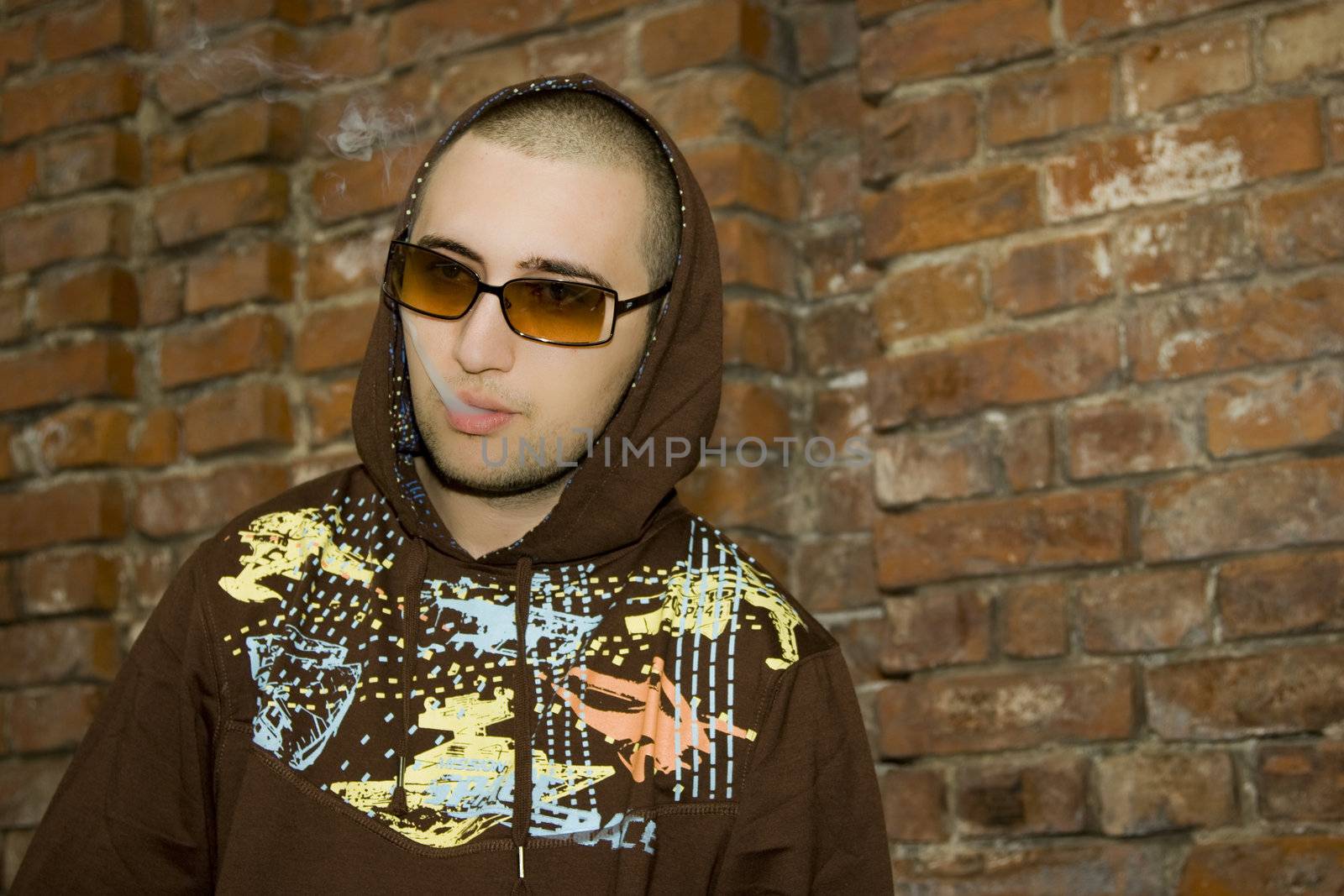 Rapper boy posing in front of a brick wall smoking