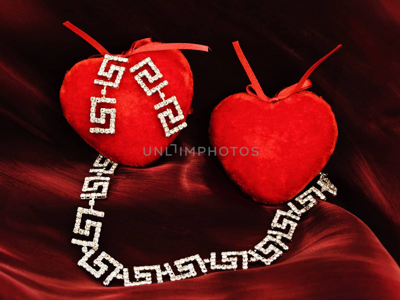 two red plush hearts with jewelry over silk
