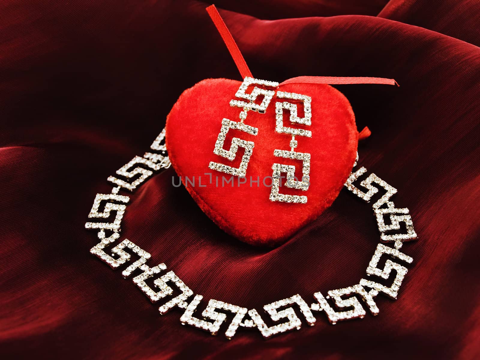 single red plush heart with jewelry over silk