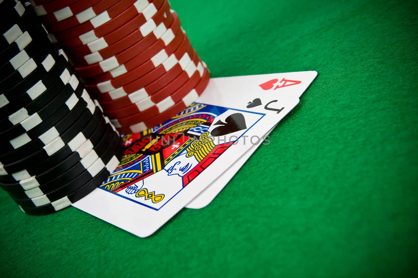Ace of hearts and black jack with stack of black and red poker chips in the background.