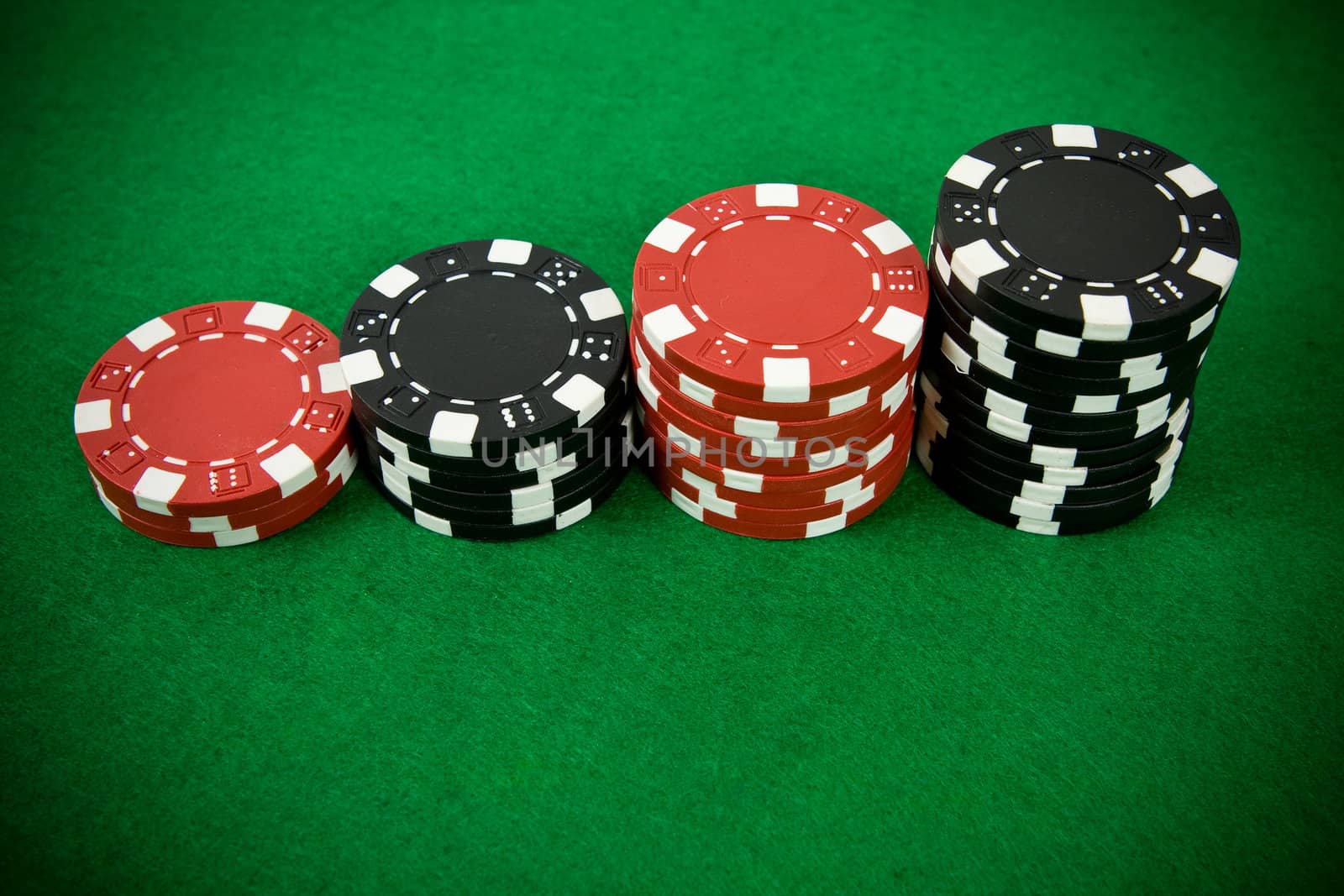Stack of black and red poker chips on green table.