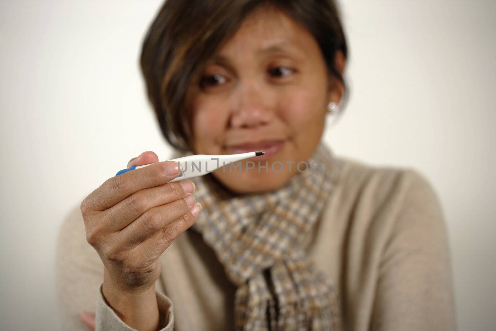 Asian female checking the temperature on a digital thermometer.  Women is out of focus - focus is on her hand and thermometer.

