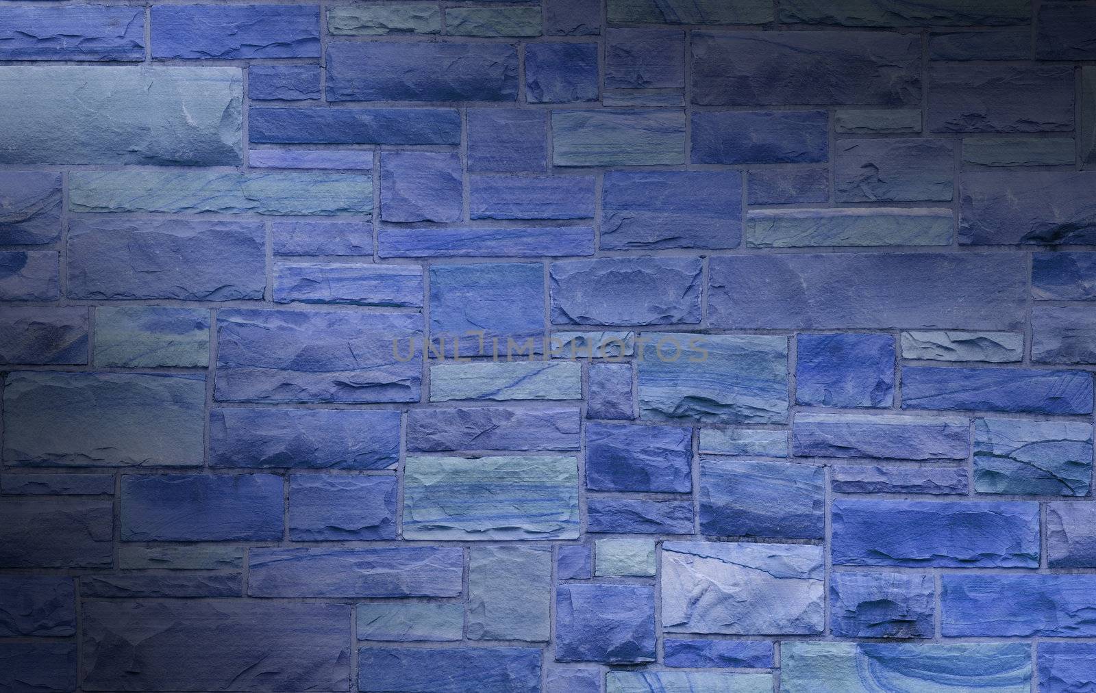 Blue masonry wall with irregular size rectangular stones dramatically lit diagonally