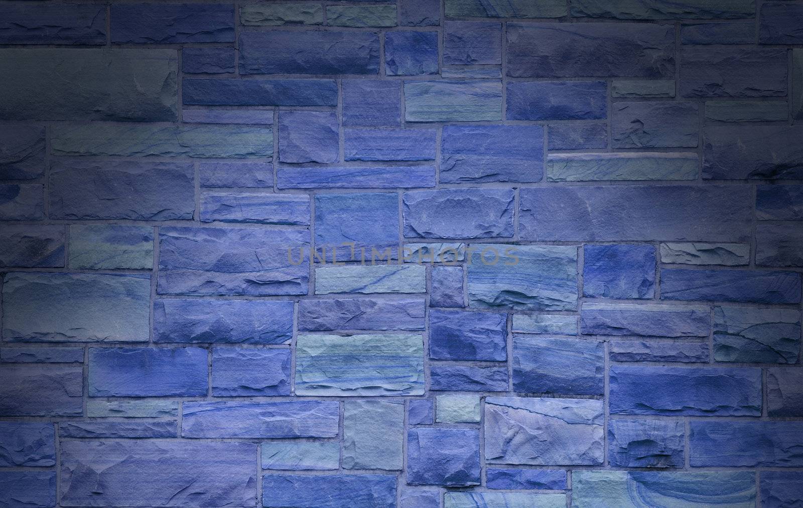 Blue masonry wall with irregular size rectangular stones dramatically lit from above