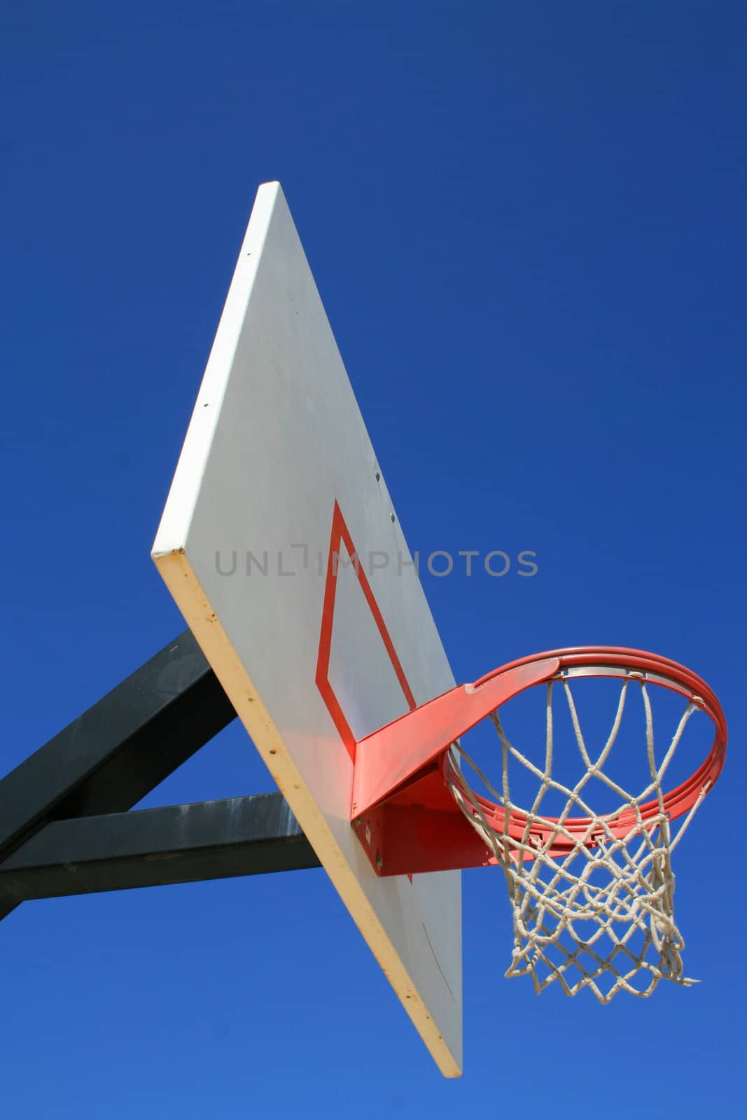 Basketball net and backboard over clear blue sky.
