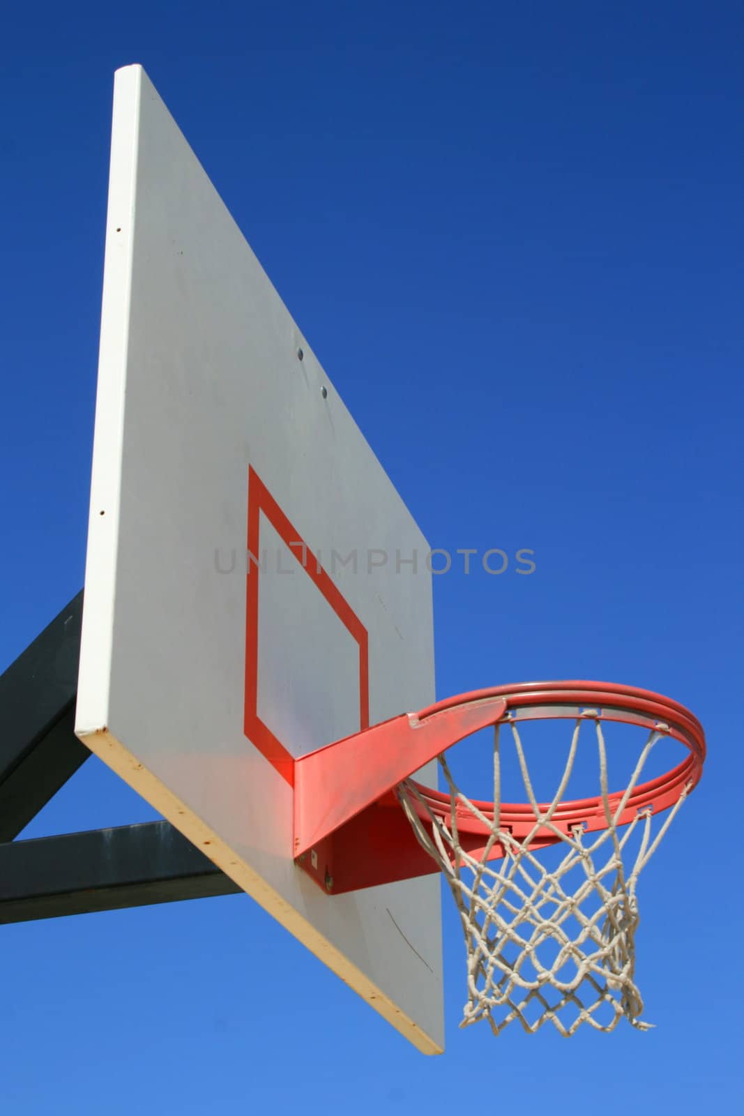 Basketball net and backboard over clear blue sky.
