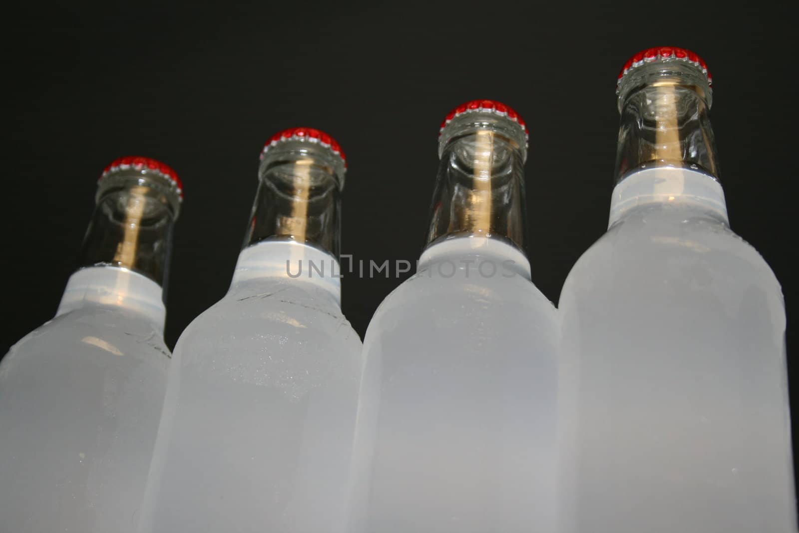 Ice cold glass bottles lined up over black background.
