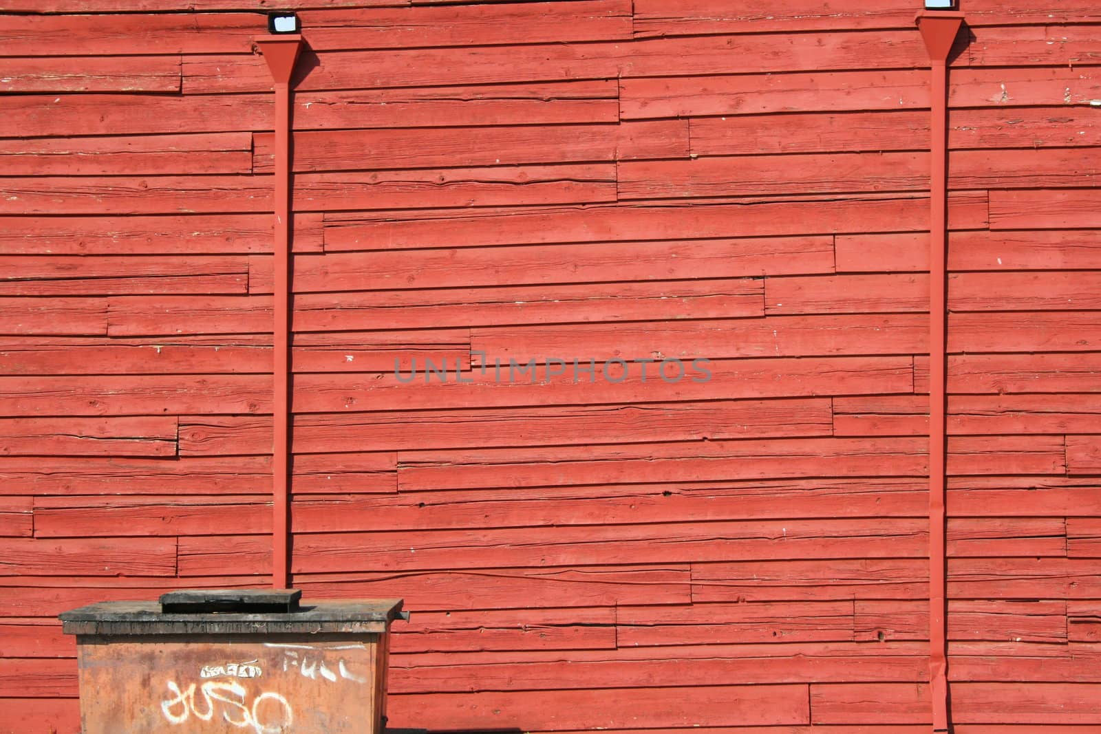 Urban part of a town showing red color wood board wall and graffiti on a garbage can.
